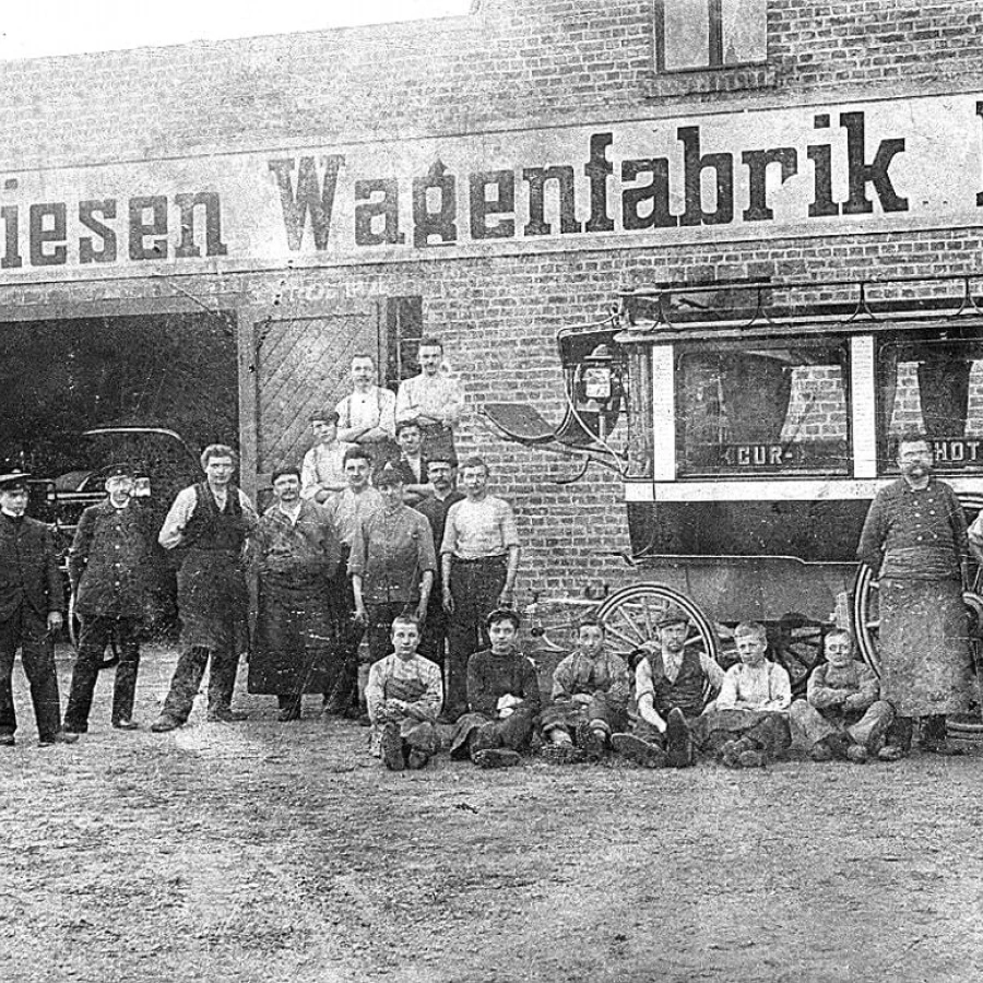 Altes Gruppenfoto vor der „Miesen Wagenfabrik Bonn“ mit dutzenden Mitarbeitenden und einer historischen Kutsche.