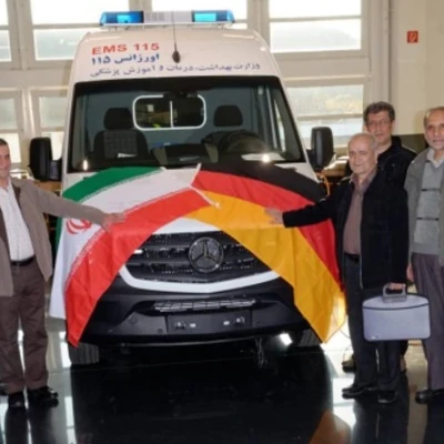 Gruppe von Männern vor einem Rettungswagen mit iranischer und deutscher Flagge auf der Motorhaube.