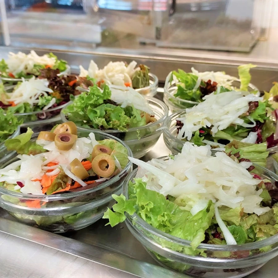 Mehrere Glasschalen mit frischen gemischten Salaten und Oliven auf einer Servierfläche.