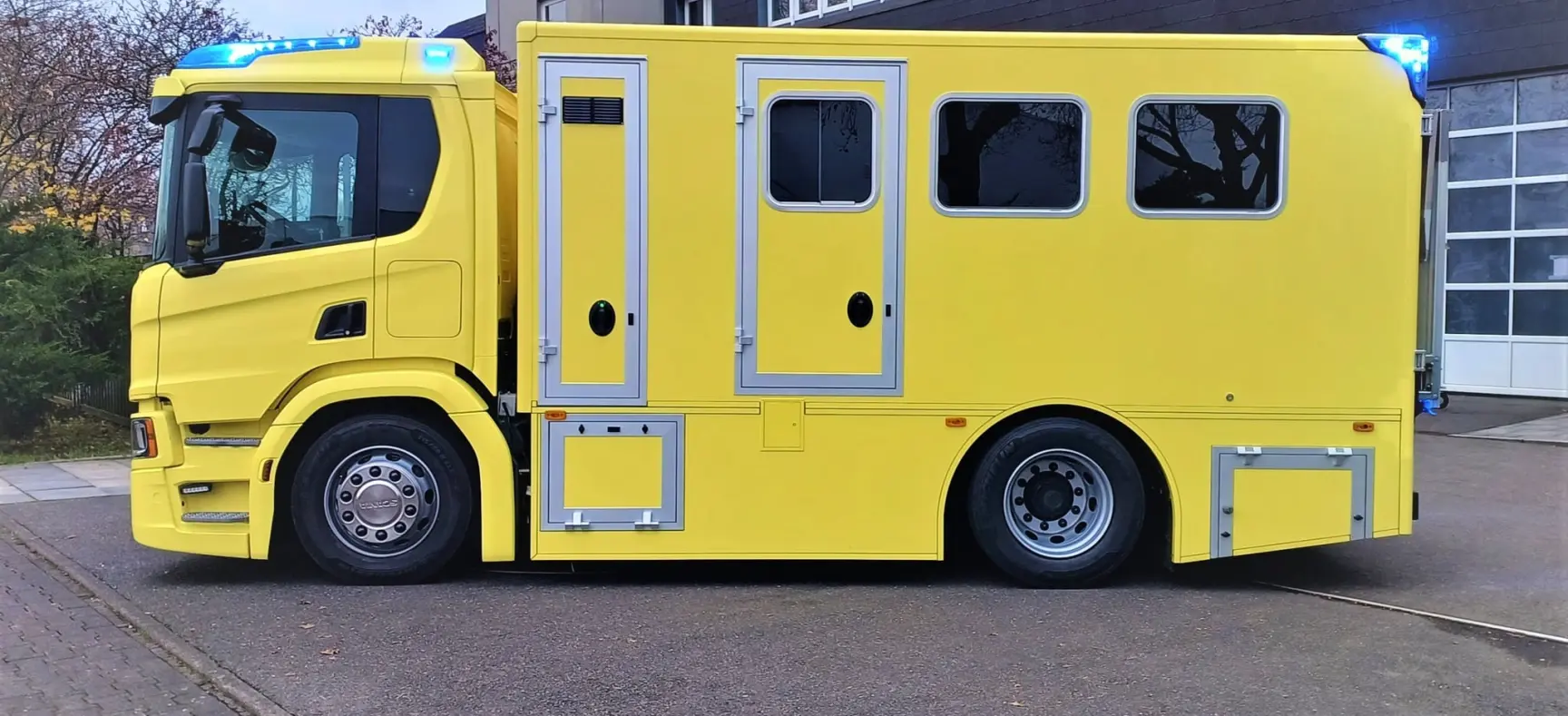 Gelber Scania-Intensivtransportwagen (ITW), seitlich aufgenommen vor Firmengebäude.