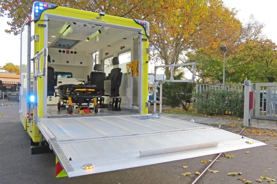 Geöffneter Heckbereich eines Sprinter-ITW mit ausgeklappter Ladebordwand und eingerollter Trage im Innenraum.