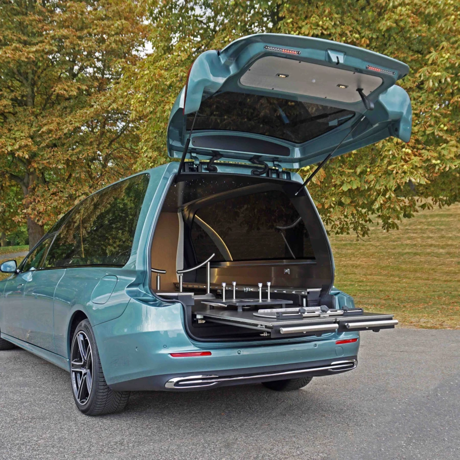 Fahrzeug mit geöffneter Heckklappe und ausziehbarem Edelstahl-Transportsystem, geparkt im Grünen.