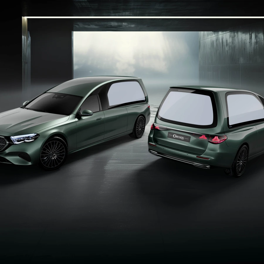 Zwei grün-metallische Bestattungswagen auf Mercedes-Basis in verde-silber, von vorn und hinten in dunkler Halle präsentiert.