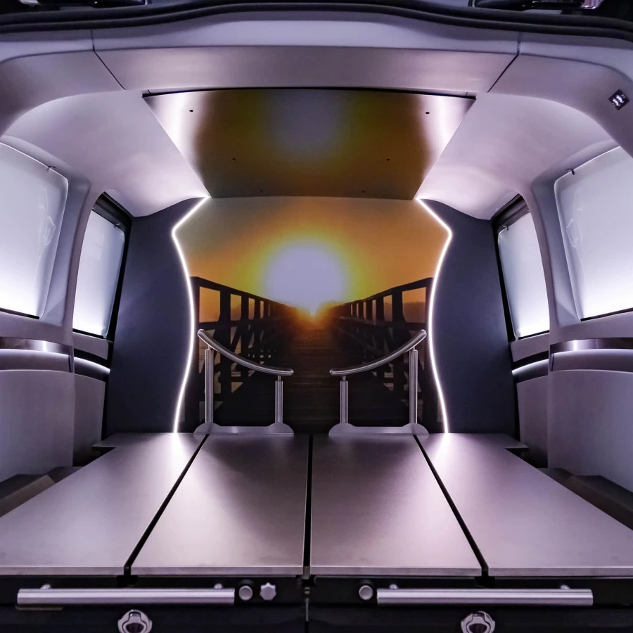 Innenansicht eines Bestattungswagens mit stilvoller LED-Beleuchtung und Sonnenuntergang-Motiv an der Stirnwand; moderne Edelstahl-Elemente und dezente Farben schaffen eine würdige Atmosphäre.