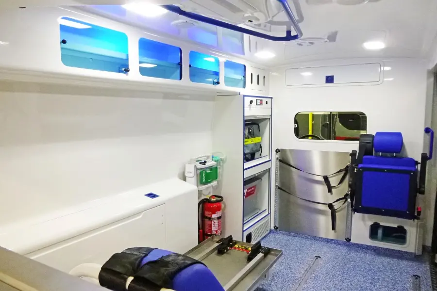 Innenraum eines modernen Rettungswagens mit blauer Beleuchtung, Sitzplätzen und Stauraum für medizinisches Equipment.