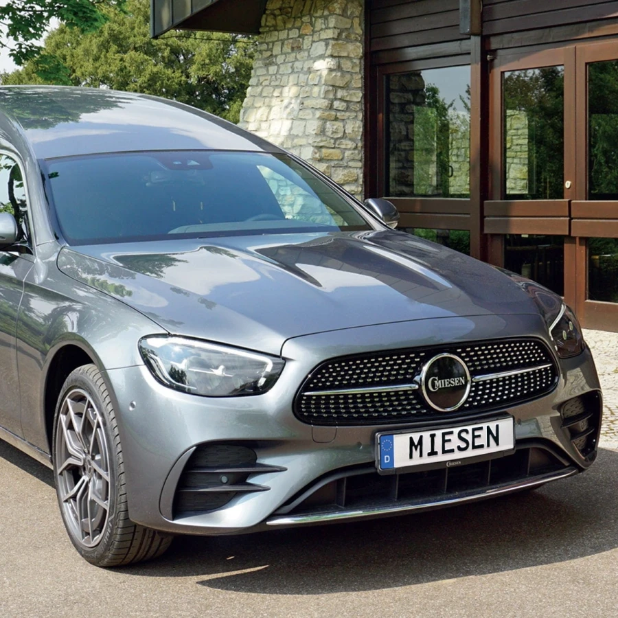 Bestattungswagen auf Basis der Mercedes E-Klasse, Modell „BONNA B2 (BR214)“, in Hightechsilber vor Gebäude mit Natursteinfassade.