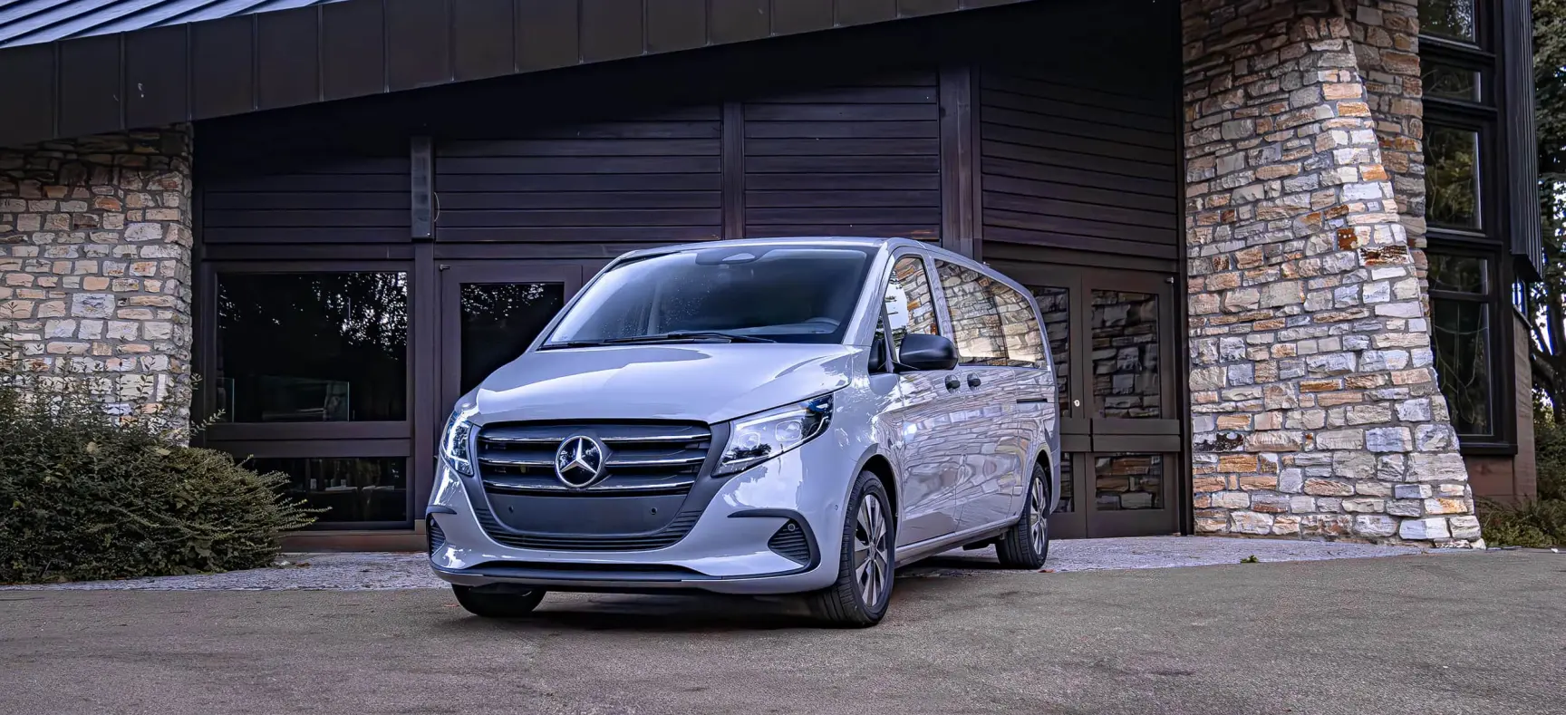 Silberner Bestattungswagen vor Gebäude mit Natursteinfassade.