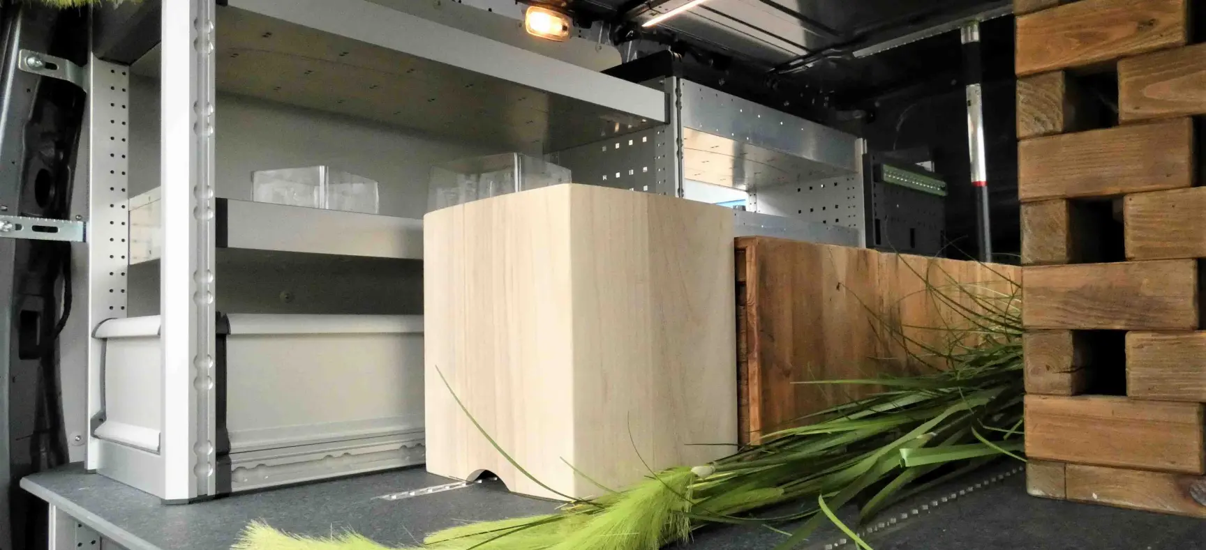 Innenraum eines Fahrzeugs mit Regalsystem, Holzelementen und Dekoration aus künstlichen Pflanzen.