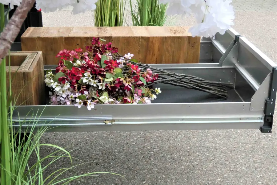 Ausgezogene Ladefläche mit Blumendekoration und Holzblöcken in einem Bestattungsfahrzeug.