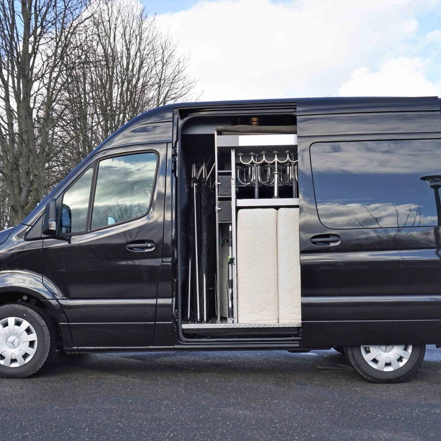Schwarzer Mercedes-Transporter mit geöffneter Schiebetür und Einblick in den Innenausbau mit silbernen Halterungen und gepolsterten Elementen.