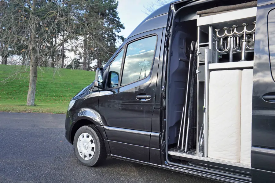 Schwarzer Bestattungswagen mit geöffneter Schiebetür und sichtbarer Innenausstattung für den Transport.
