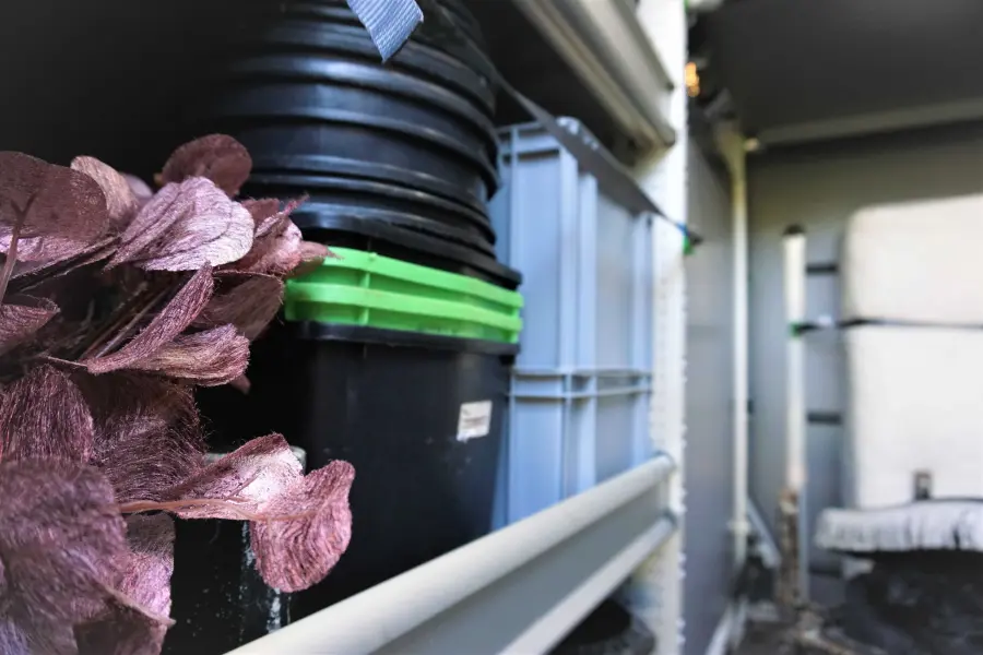 Detailaufnahme eines Fahrzeugregals mit schwarzen Eimern, grauen Kisten und violetten Dekoelementen.