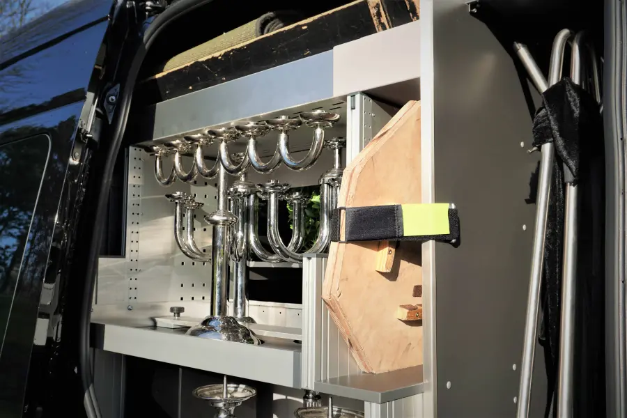 Seitliches Staufach eines Bestattungsfahrzeugs mit gesicherten silbernen Kerzenständern und Ablagen.