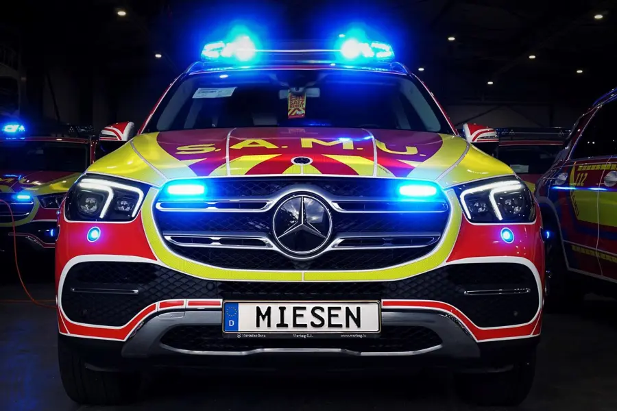 Frontansicht eines rot-gelben Einsatzfahrzeugs mit eingeschaltetem Blaulicht in einer Halle.