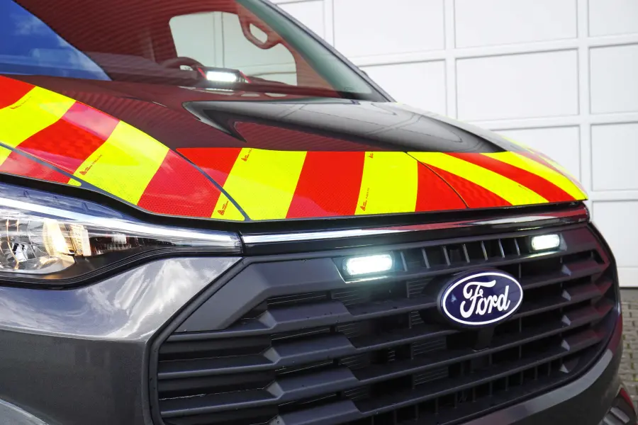 Frontansicht eines Ford-Einsatzfahrzeugs mit gelb-roter Warnbeklebung und eingeschalteter LED-Frontblitzleuchte.