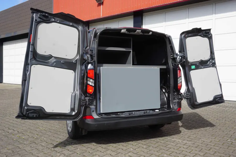 Geöffnetes Heck eines schwarzen Transporters mit integriertem Stauraum- und Klappsystem vor einer Garagenfront.