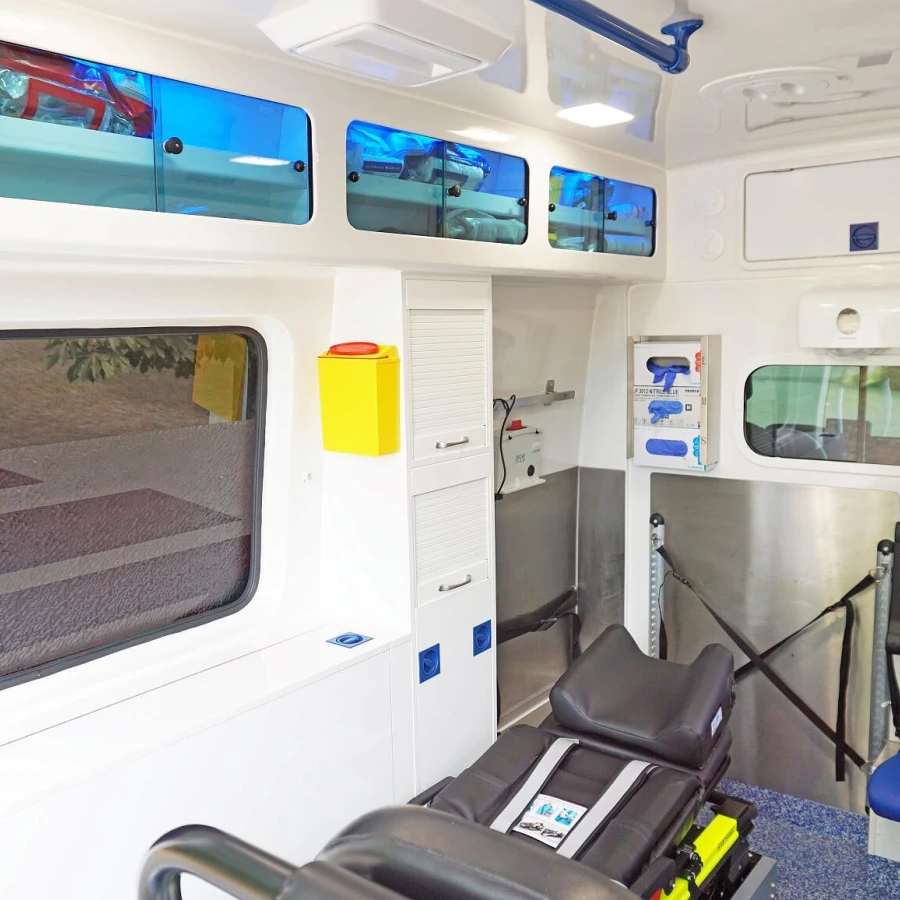 Innenraum eines modernen Krankentransportwagens mit blauer Sitzbank, medizinischer Liege und weißen Staufächern mit blauen Glastüren.