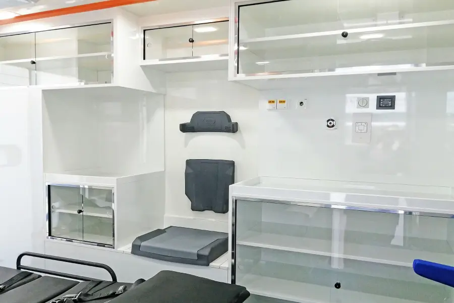 Innenraum eines RTW mit gepolsterten Sitzflächen, Glasvitrinen und medizinischen Anschlüssen an der Wand.