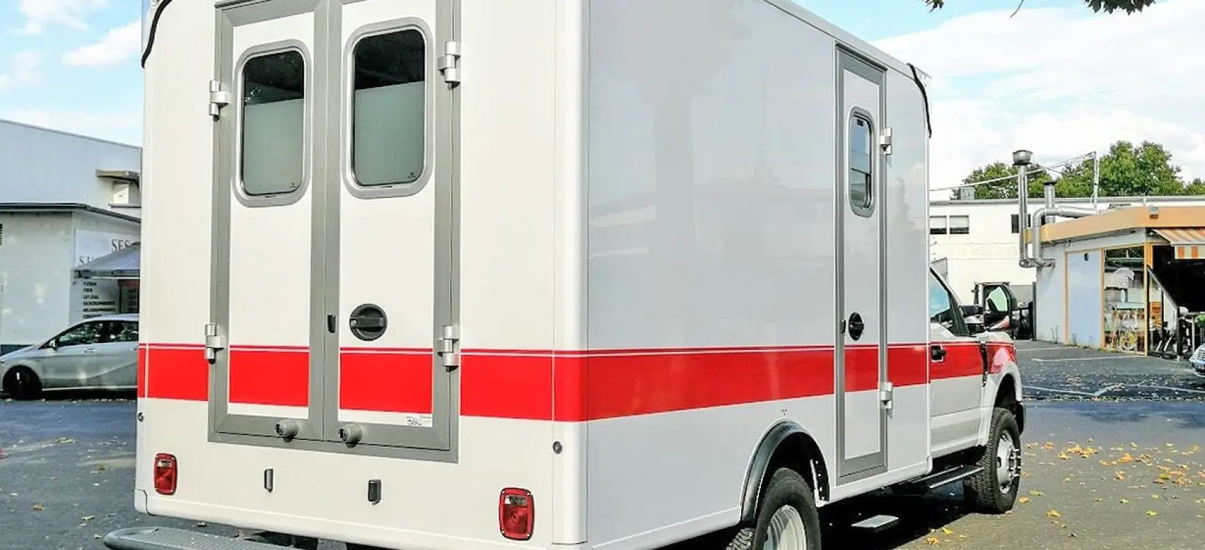 Kastenförmiger Rettungswagen mit rotem Streifen auf Parkplatz.