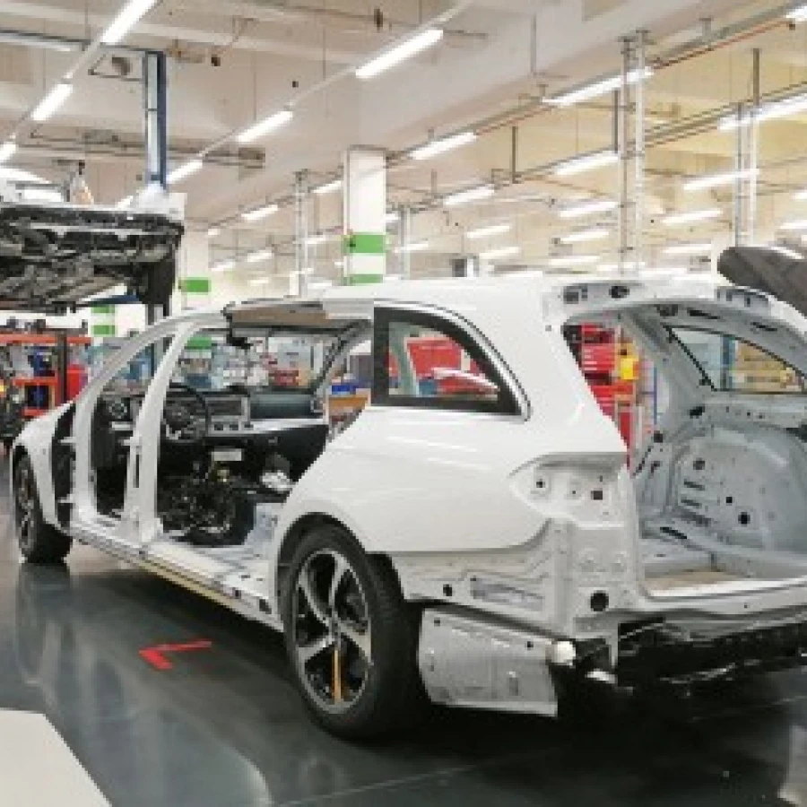 Fertigung eines Bestattungswagens in einer Produktionshalle, Karosserie im Rohbau auf dem Werkstattboden, ein weiteres Fahrzeug auf einer Hebebühne im Hintergrund.