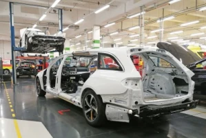 Fertigung eines Bestattungswagens in einer Produktionshalle, Karosserie im Rohbau auf dem Werkstattboden, ein weiteres Fahrzeug auf einer Hebebühne im Hintergrund.