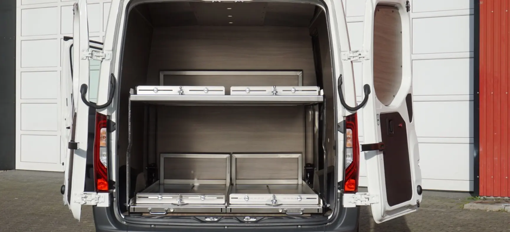 Geöffnete Hecktüren eines weißen Fahrzeugs mit modernem Innenausbau und zwei übereinander angeordneten Ladeflächen aus Edelstahl.