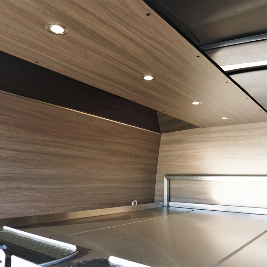 Innenraum eines Fahrzeugs mit holzverkleideten Wänden und Decke sowie integrierter LED-Beleuchtung.