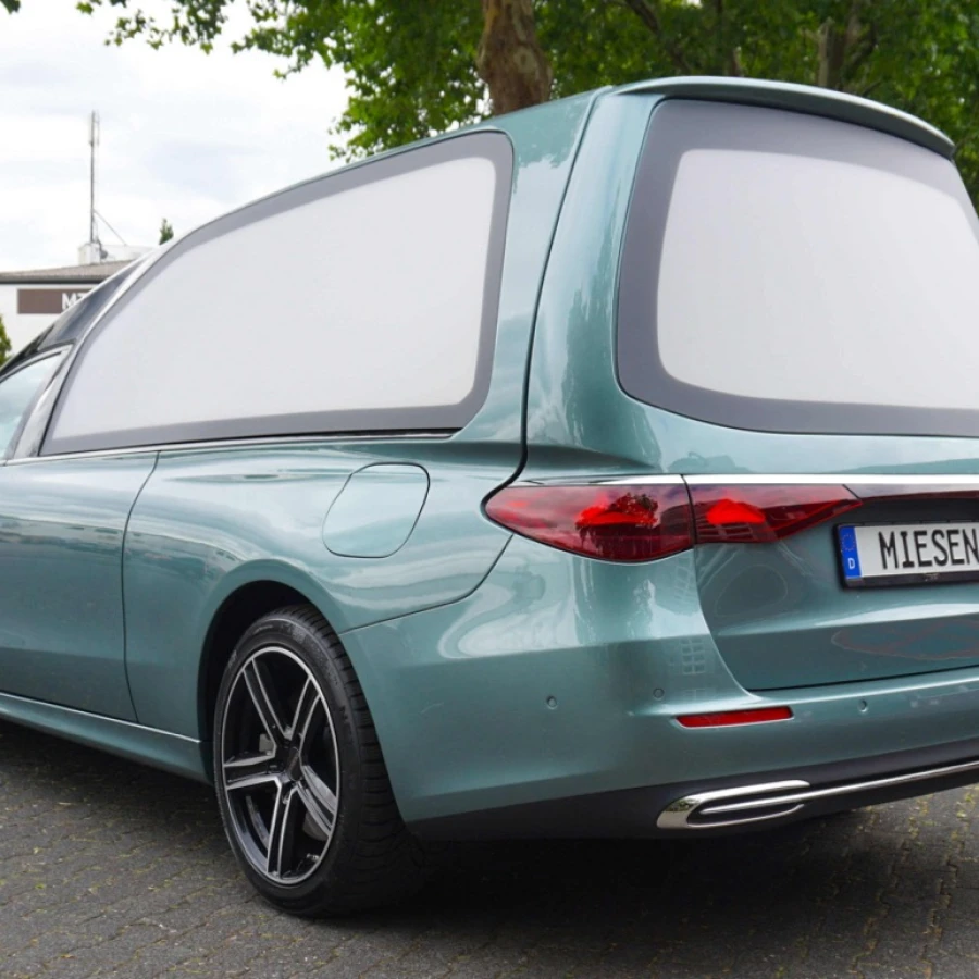 Eleganter, türkisfarbener Bestattungswagen mit MIESEN-Kennzeichen, geparkt auf einer Straße im Grünen.