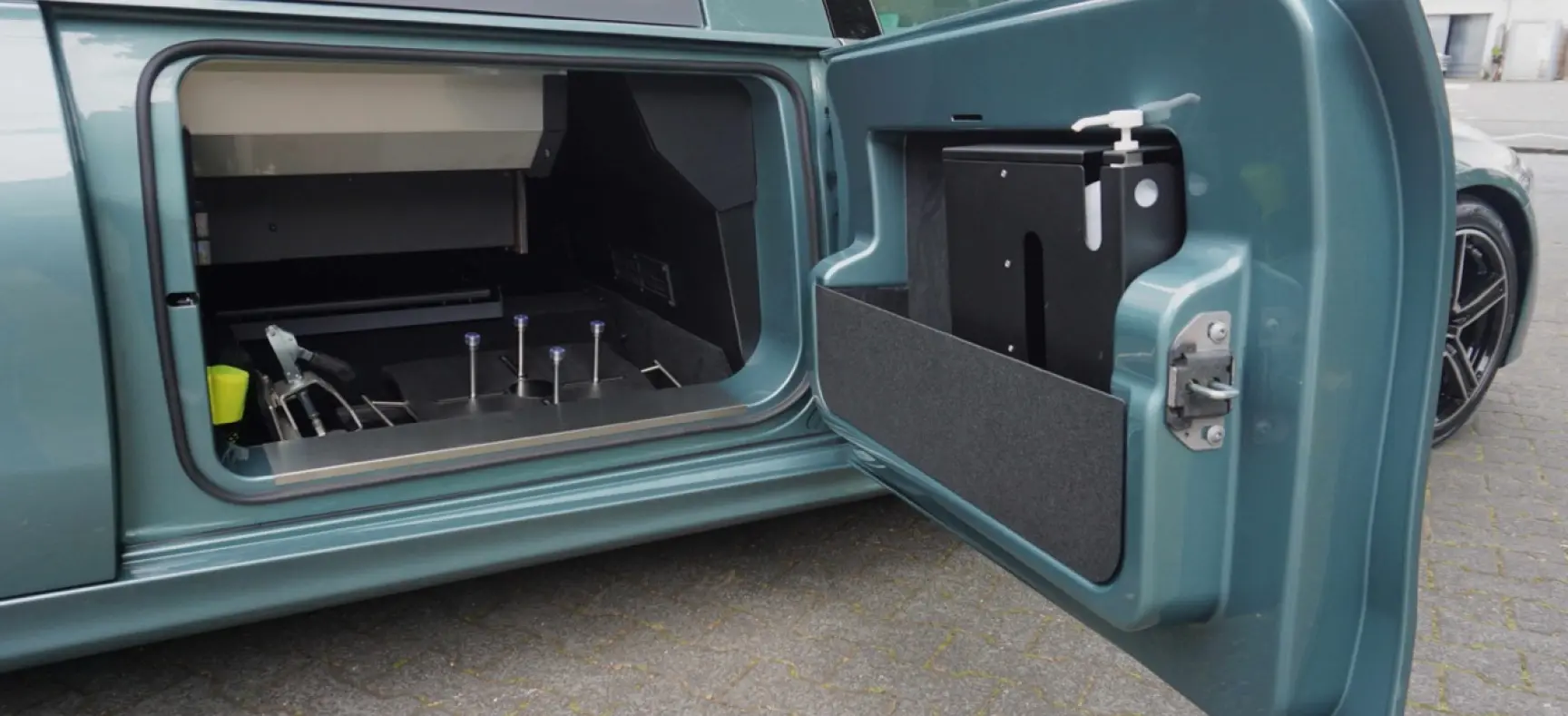 Seitlich geöffneter Stauraum eines Bestattungsfahrzeugs mit integriertem Handdesinfektionsspender in der Tür.