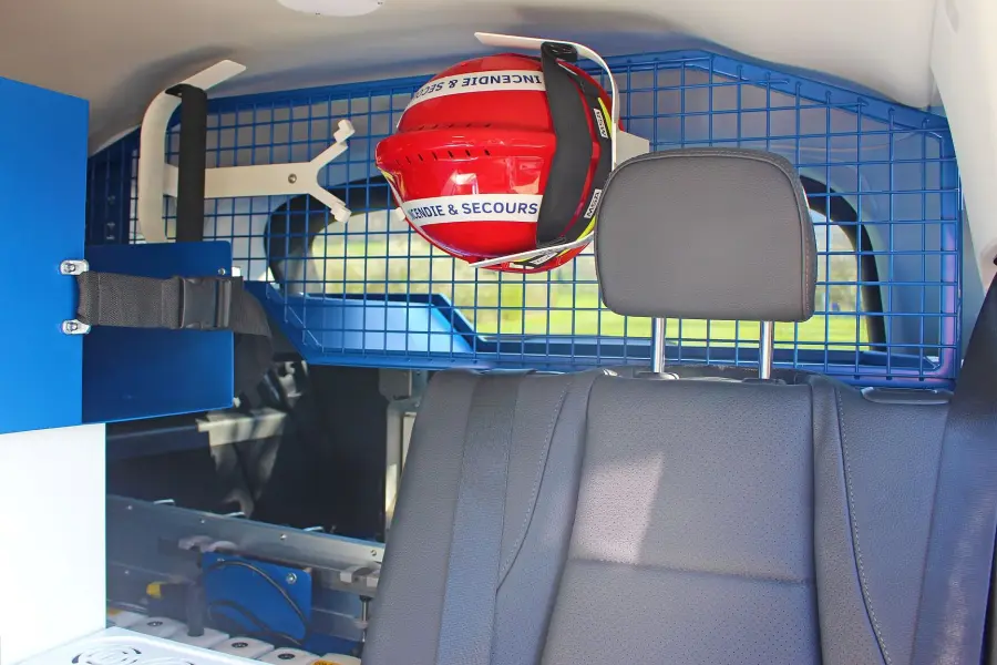 Innenraum eines Einsatzfahrzeugs mit Sitzbank, rotem Feuerwehrhelm und blauer Gittertrennwand.