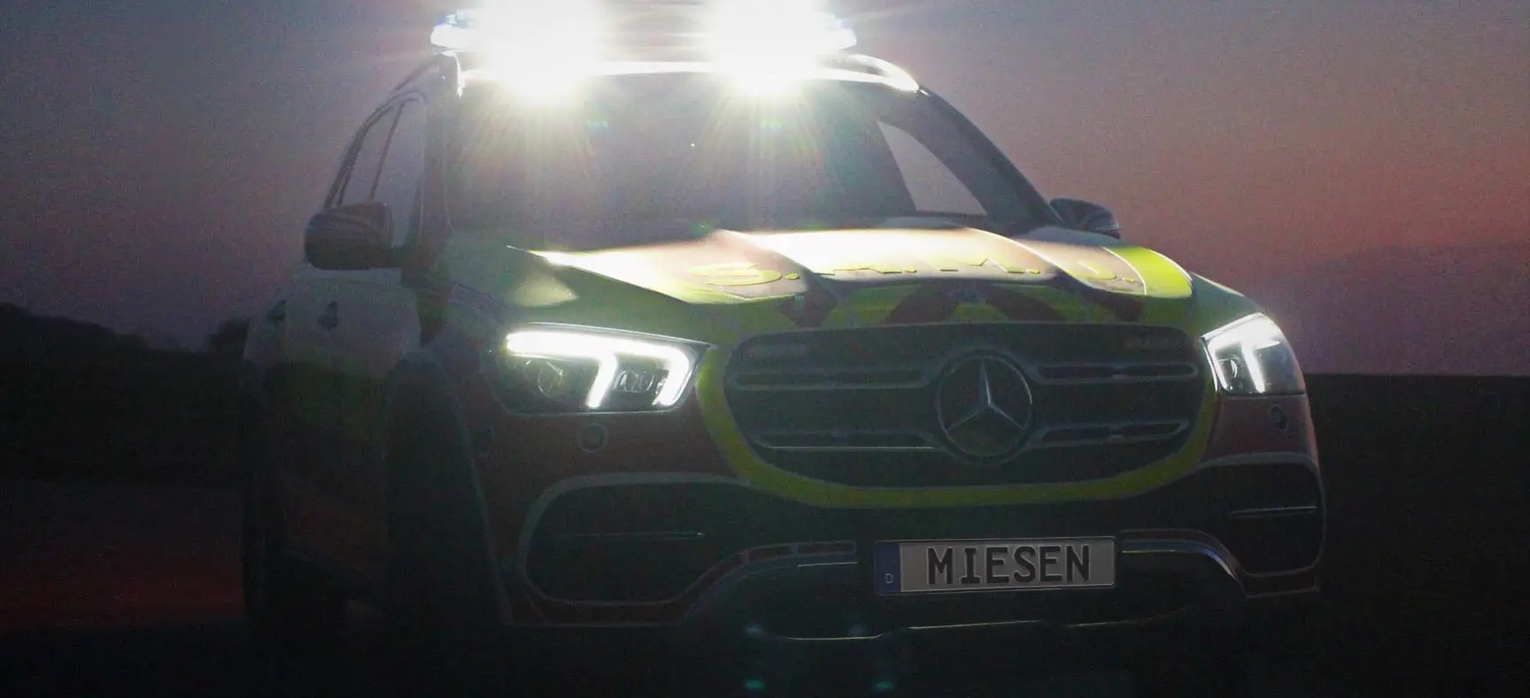 Einsatzfahrzeug von MIESEN bei Nachtaufnahme mit eingeschalteten Blaulichtern und hellen Frontscheinwerfern.
