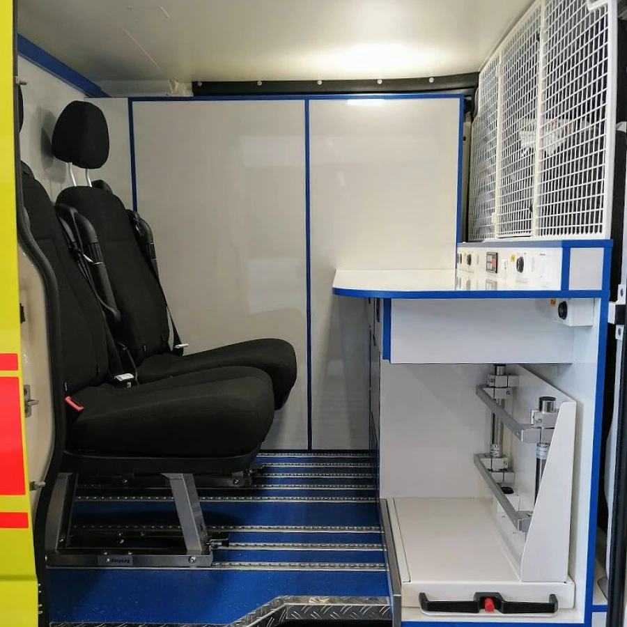 Innenraum eines Krankenwagens mit zwei Sitzen, seitlichem Arbeitstisch und Stauraum im medizinischen Bereich.