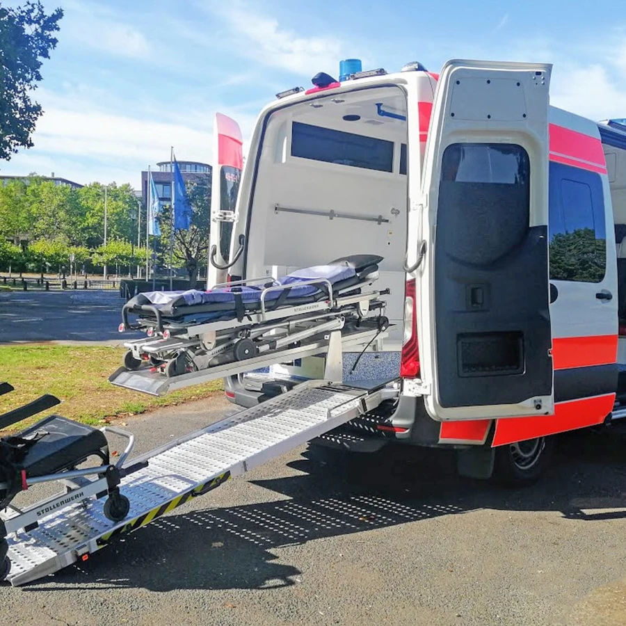 Rettungswagen mit geöffneter Hecktür, ausgefahrener Trage und verlängerter Laderampe im Außenbereich.