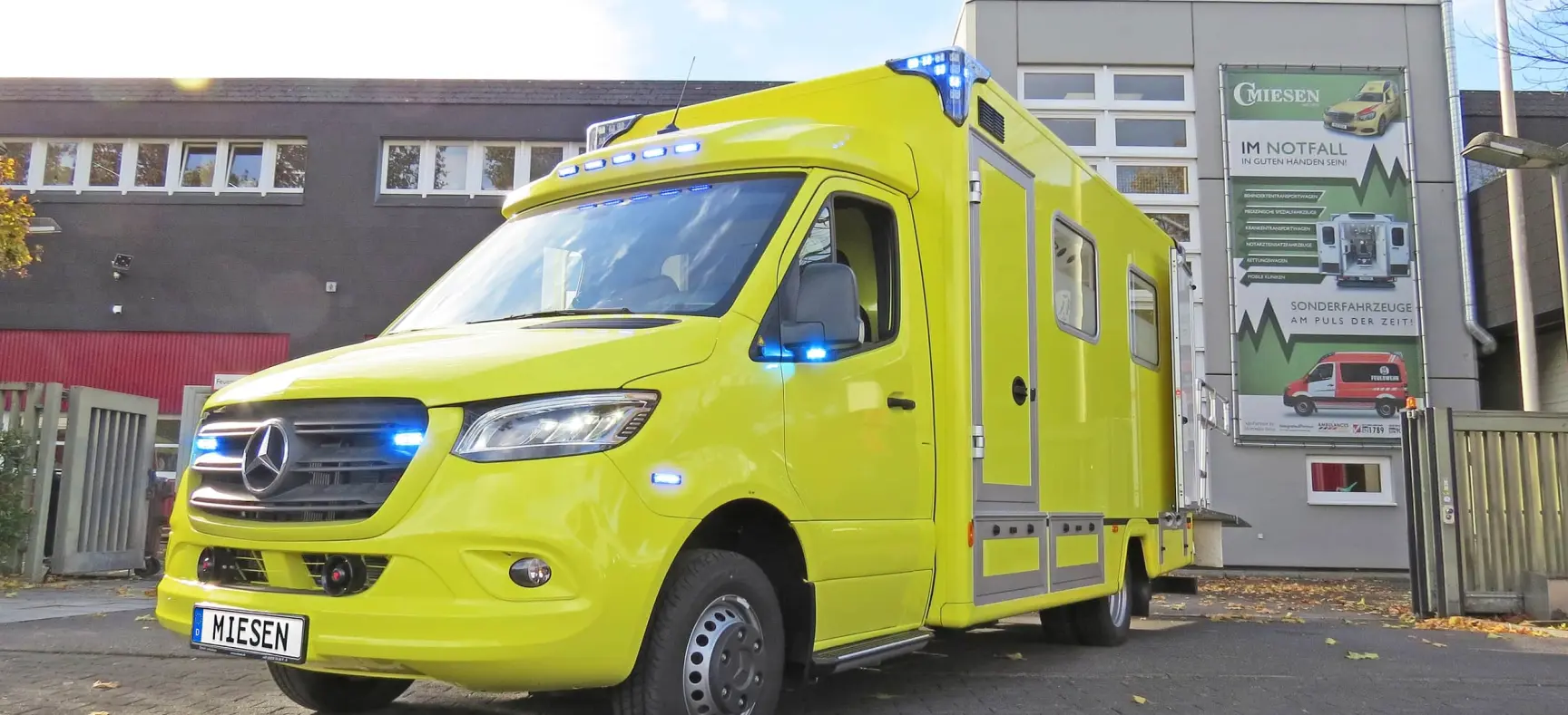 Gelber Intensivtransportwagen (ITW) auf Mercedes-Sprinter-Basis mit blauen LED-Signalleuchten vor dem Firmengebäude von Miesen.