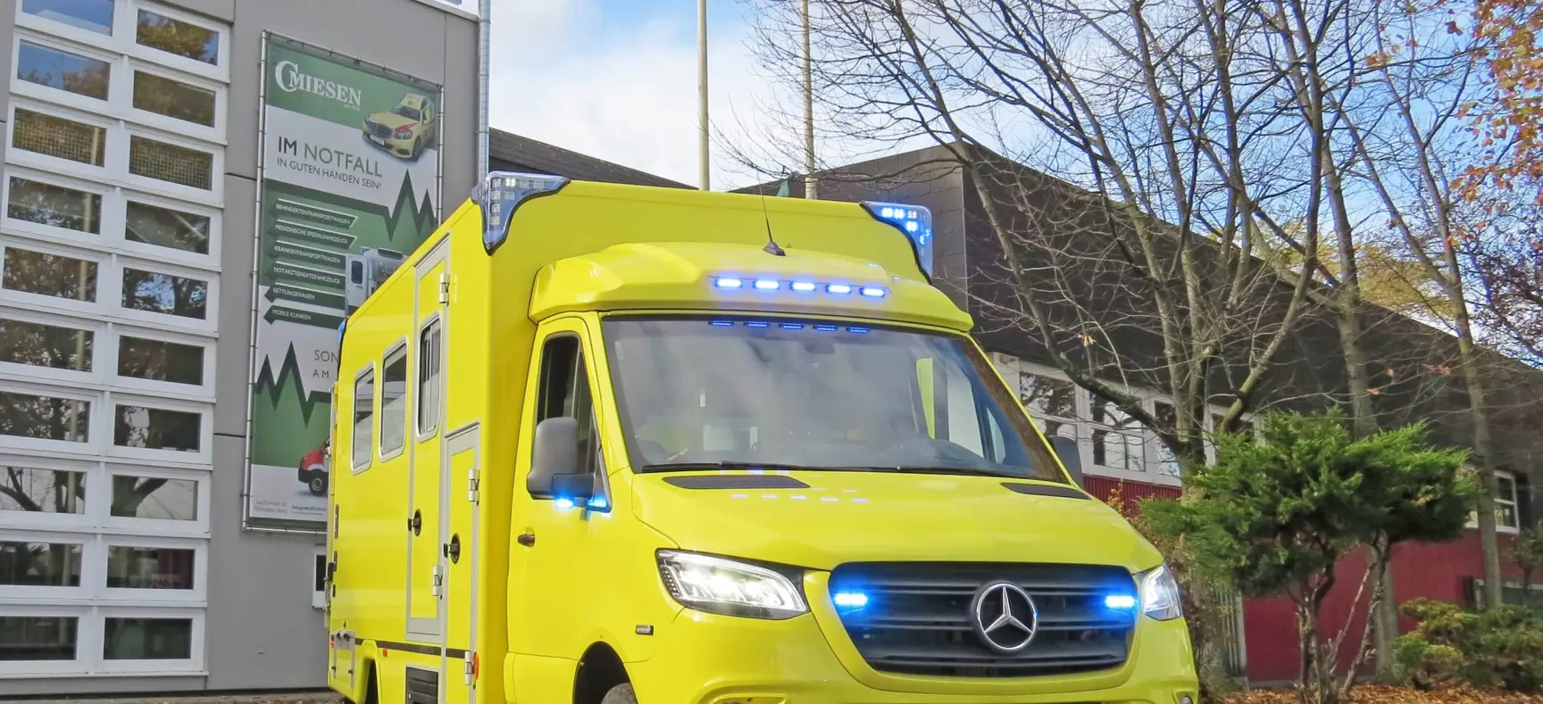 Frontansicht eines gelben ITW auf Mercedes-Sprinter-Basis mit eingeschaltetem Blaulicht vor dem Miesen-Firmengebäude an einem herbstlichen Tag.