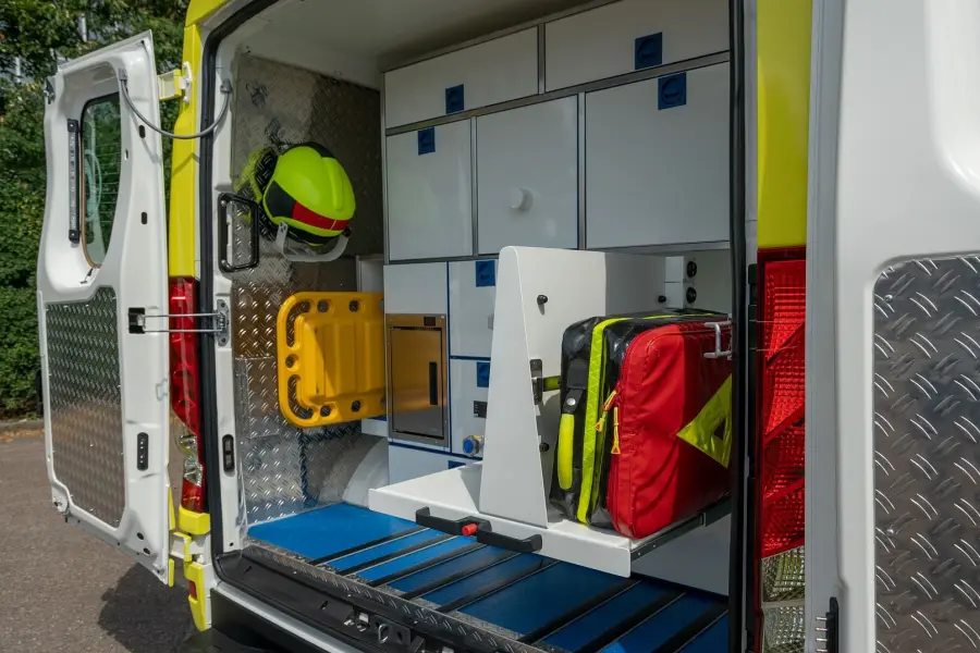 Blick in das geöffnete Heck eines gelben Notarztfahrzeugs mit ausziehbarem Stauraum, Rettungsrucksack und montiertem Helmhalter.