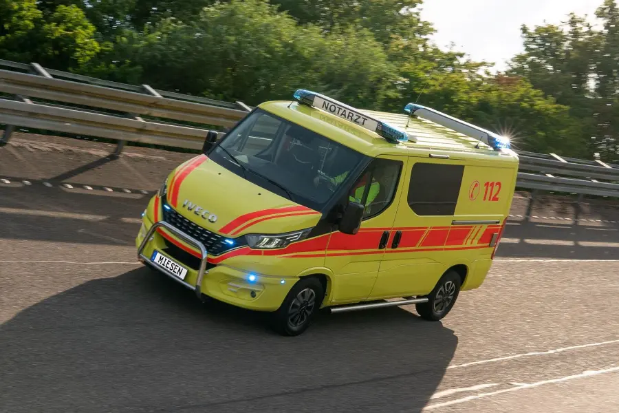 Gelbes Notarztfahrzeug auf der Straße mit roter und gelber Warnbeklebung und eingeschaltetem Blaulicht.