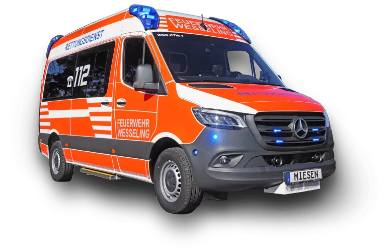 Rettungswagen der Feuerwehr Wesseling auf Mercedes-Benz-Basis mit roter und weißer Beklebung sowie eingeschalteten Blaulichtern.