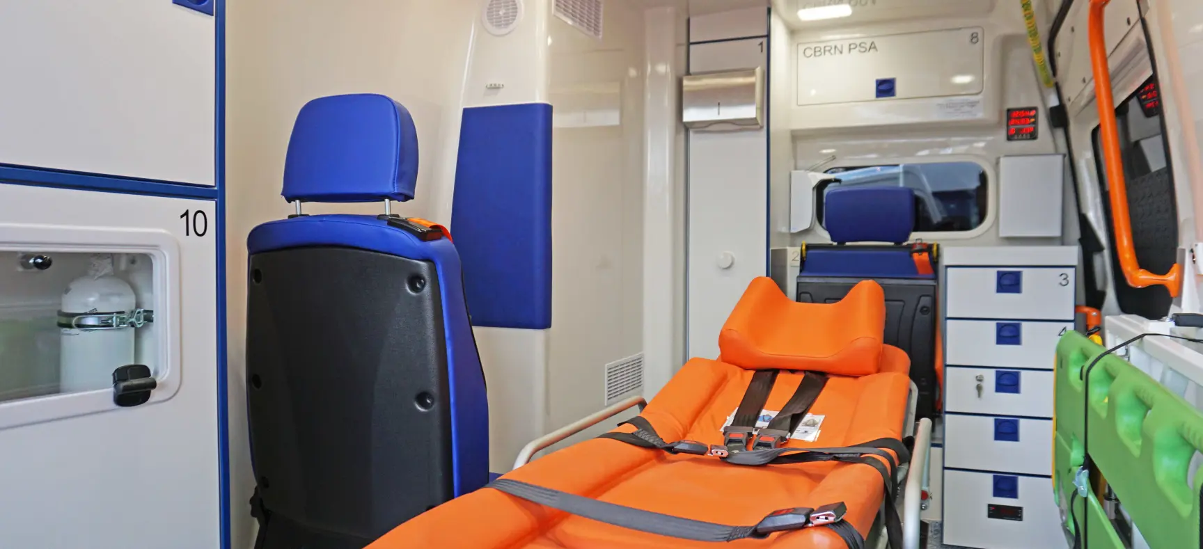 Innenraum eines Rettungswagens mit oranger Krankentrage, blauen Sitzen und medizinischen Schränken.
