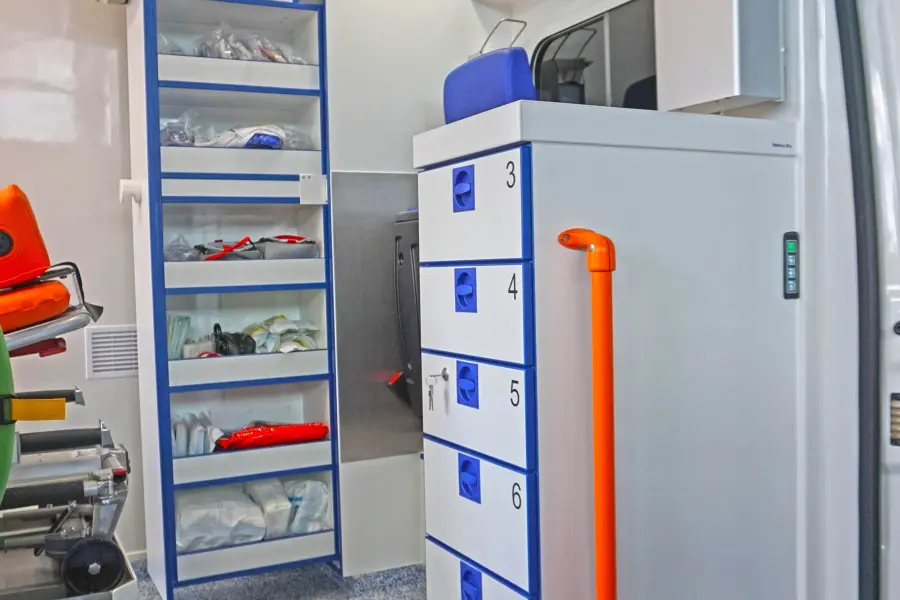 Innenansicht eines KTW B mit offener Regaleinheit, nummerierten Schubladen, oranger Griffstange und gelbem Unterlegkeil.