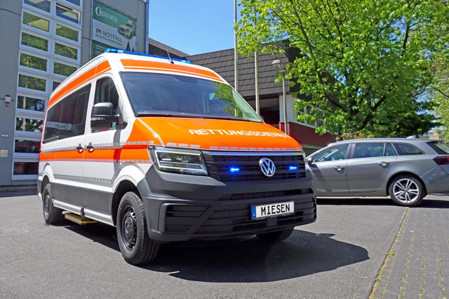 KTW auf VW Crafter-Basis mit orangener RETTUNGSDIENST-Beklebung und Blaulichtanlage, aufgenommen vor dem Gebäude der Firma Miesen.