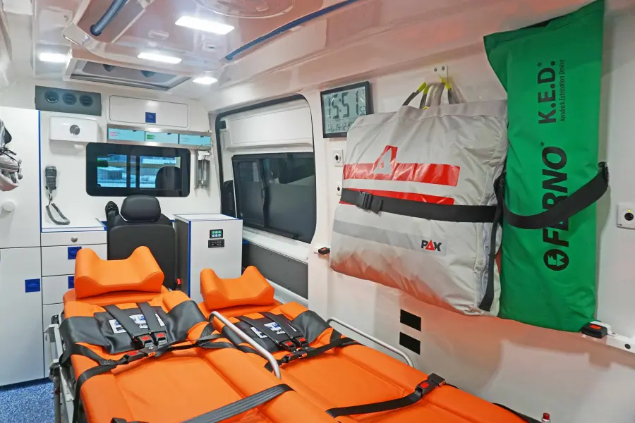 Innenraum eines Rettungswagens mit orangefarbener Trage, Notfallausrüstung und medizinischen Geräten.