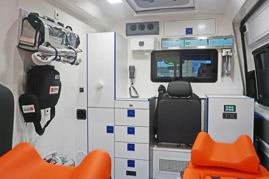 Innenraum eines modernen Rettungswagens mit medizinischer Ausstattung, Schränken und oranger Liege.