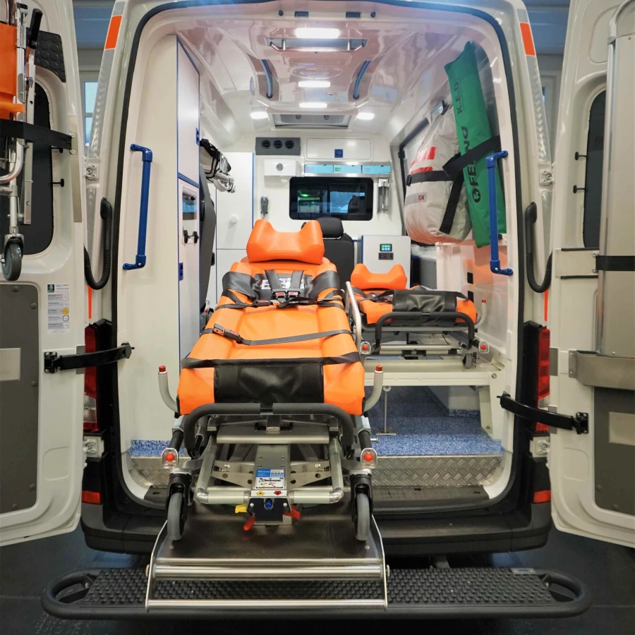 Blick in den geöffneten Innenraum eines modernen Rettungswagens mit leuchtend orangefarbener Trage und medizinischer Ausstattung.