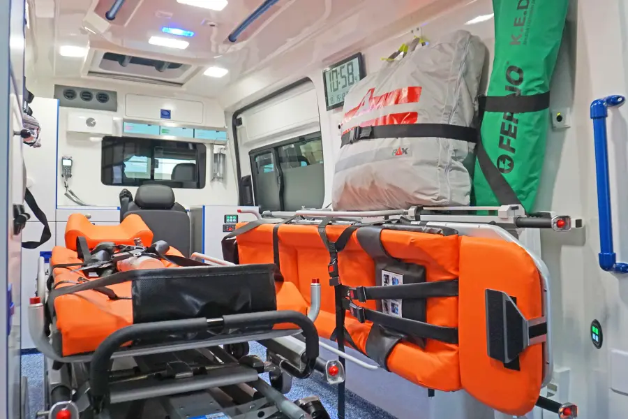 Innenraum eines Rettungswagens mit orangefarbener Trage, Notfallausrüstung und medizinischen Geräten.