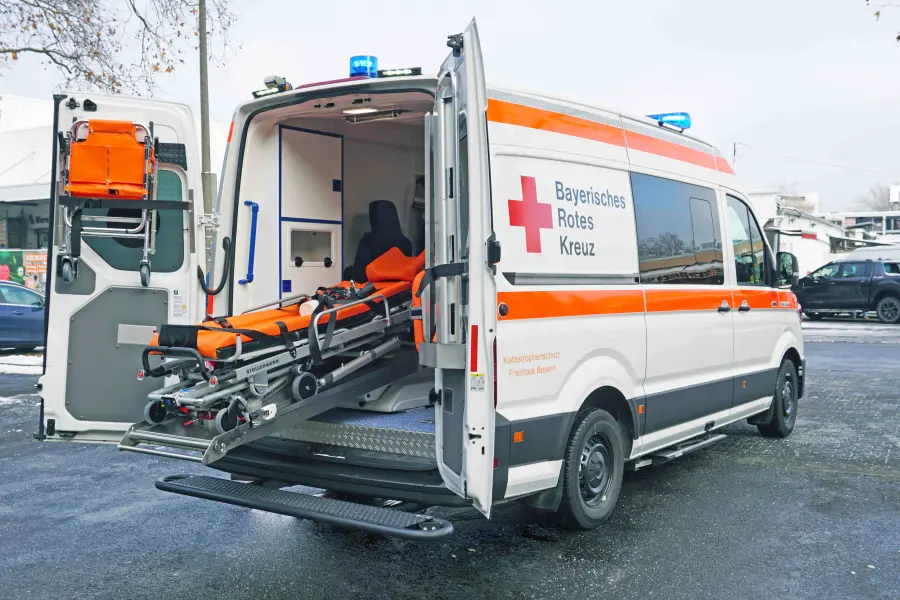 Rettungswagen des Bayerischen Roten Kreuzes mit geöffneter Heckklappe und ausgefahrener Trage.
