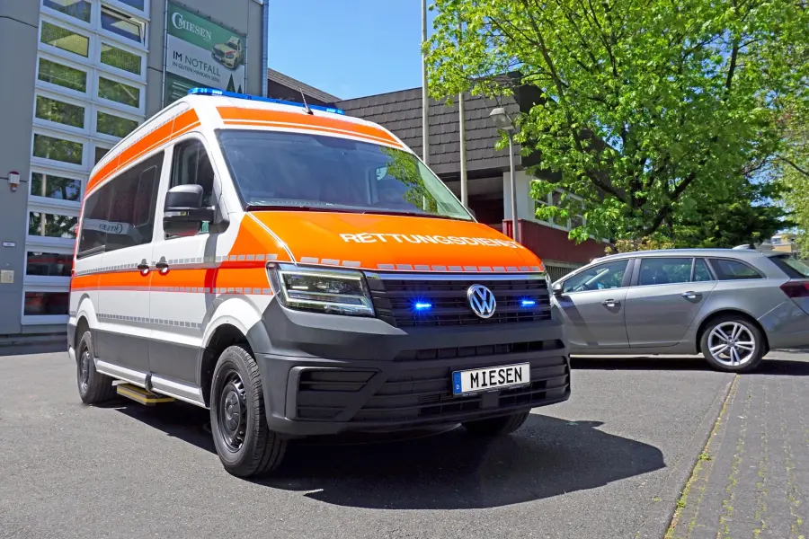 KTW auf VW Crafter-Basis mit orangener RETTUNGSDIENST-Beklebung und Blaulichtanlage, aufgenommen vor dem Gebäude der Firma Miesen.