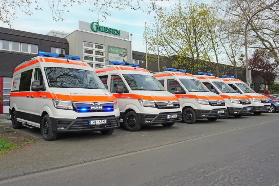 Mehrere KTW auf MAN TGE-Basis mit BRK-Beschriftung und Blaulicht, aufgereiht vor dem Firmengebäude von Miesen.