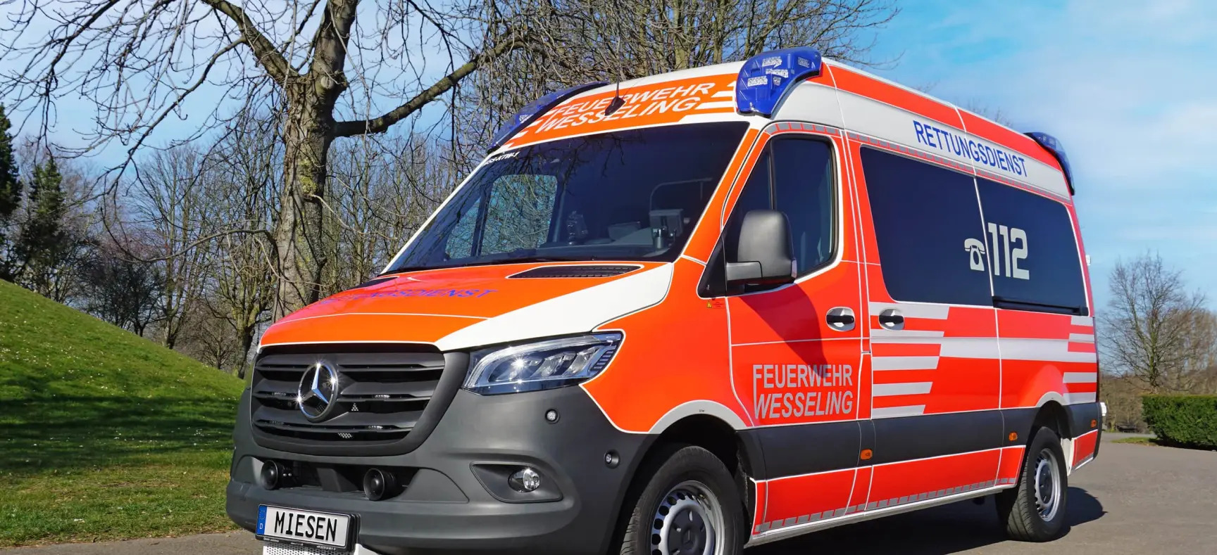 TW der Feuerwehr Wesseling auf Mercedes-Benz Sprinter-Basis mit Hochdach, auffälliger rot-weißer Beklebung und Blaulichtanlage.
