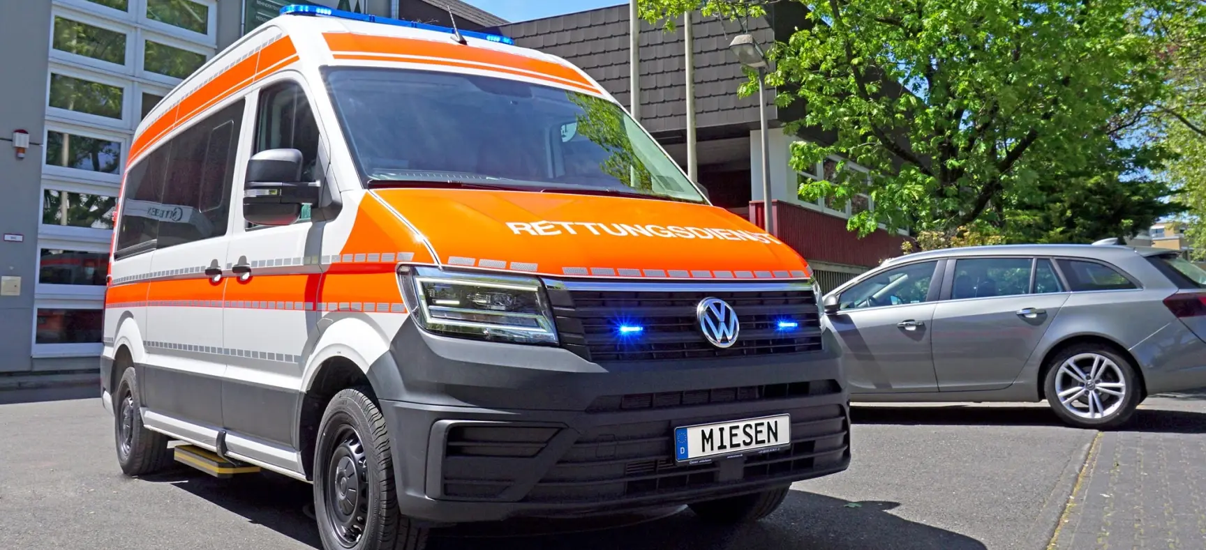 KTW auf VW Crafter-Basis mit orangener RETTUNGSDIENST-Beklebung und Blaulichtanlage, aufgenommen vor dem Gebäude der Firma Miesen.